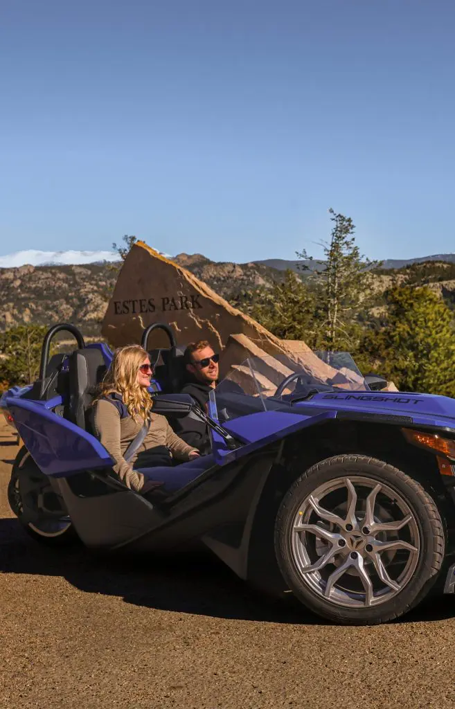 Backbone Adventures - Slingshot Rentals Page - Slingshot 1 A couple poses for a picture in front of the Welcome to Estes Park sign while in their rented Slingshot from Backbone Adventures