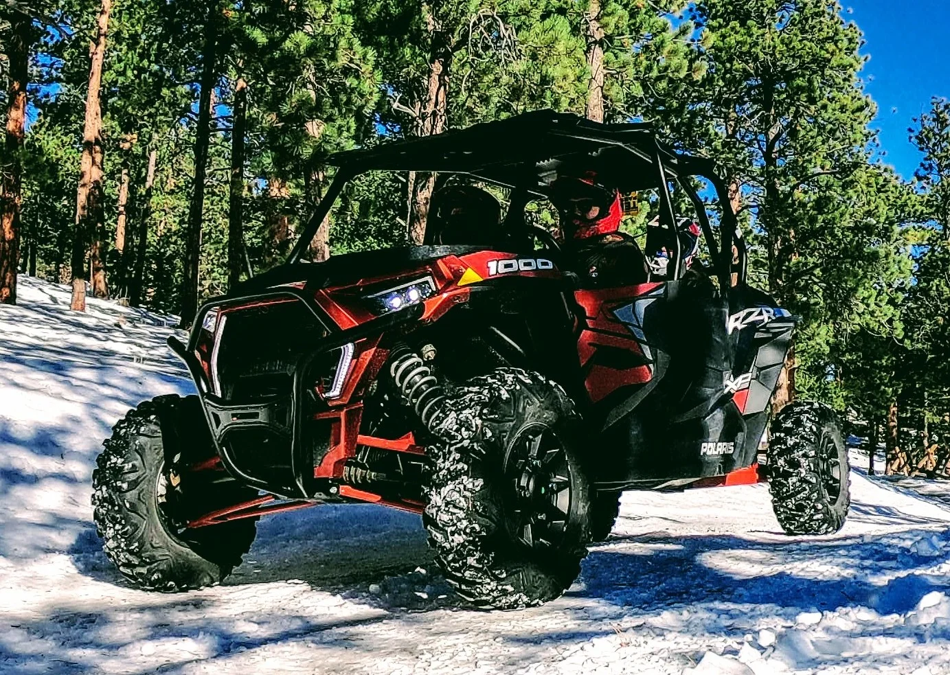 A red RZR 1000 drives through the snow. It is ready to rent at Backbone Adventures